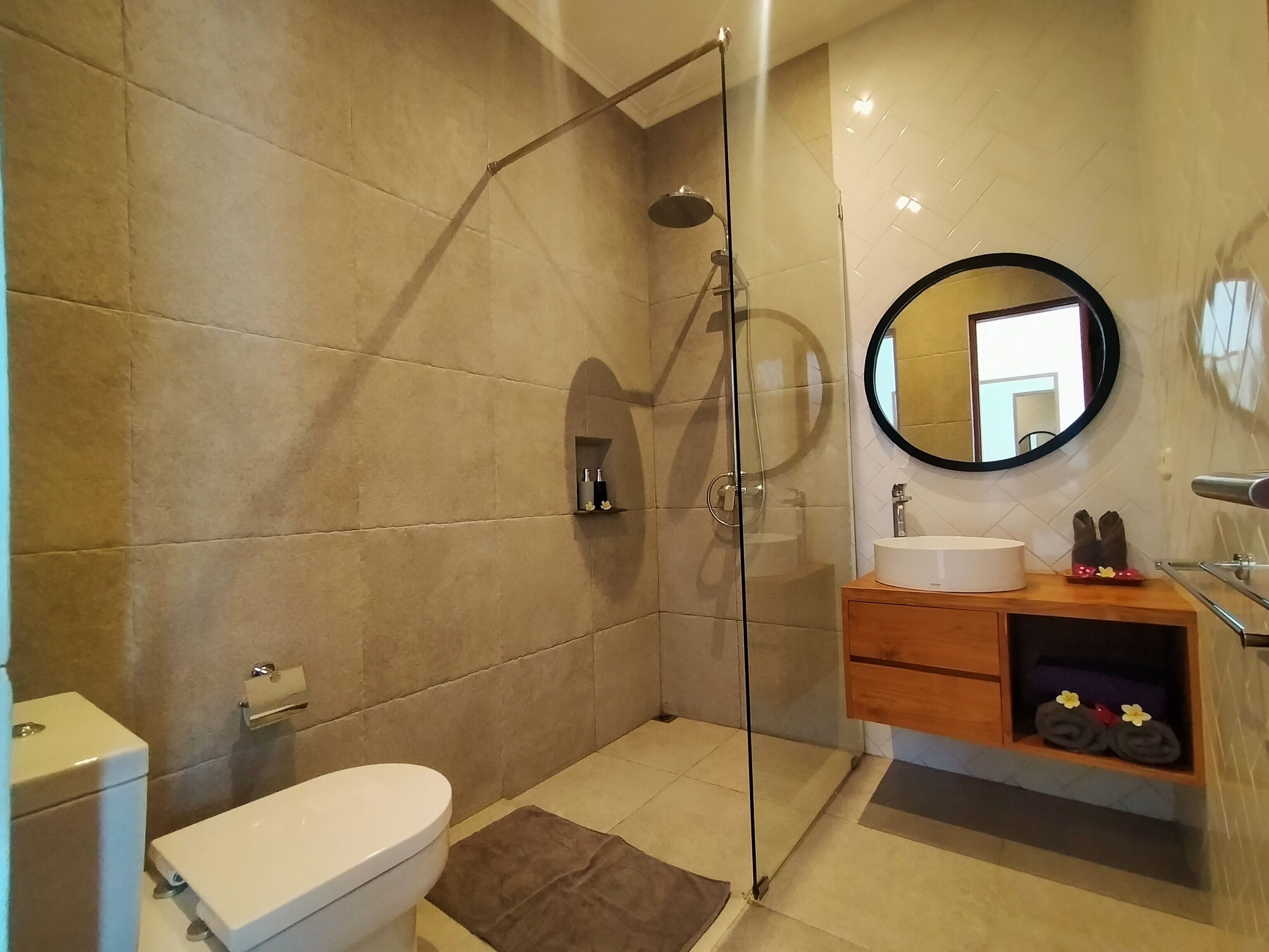 Une salle de bain moderne avec une douche à parois de verre, des toilettes, un lavabo avec un miroir et un meuble-lavabo en bois.