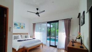 A bedroom with a bed, a ceiling fan, a wooden floor, a sliding glass door to a pool, and a small table with a vase of flowers. - Villa Ataya (Sukasada)