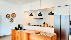 A modern kitchen with a wooden island, stainless steel appliances, pendant lighting, and decorative plates on the wall. - Villa Ataya (Sukasada)