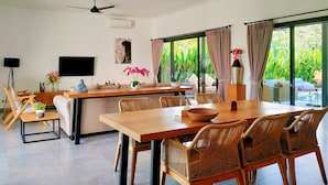 A modern living room with a dining area, large windows, and a ceiling fan. - Villa Ataya (Sukasada)