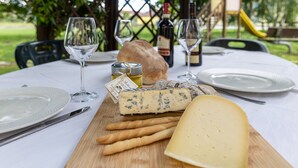 Ein gedeckter Tisch mit Käse, Brot, Wein und einer Flasche Olivenöl.