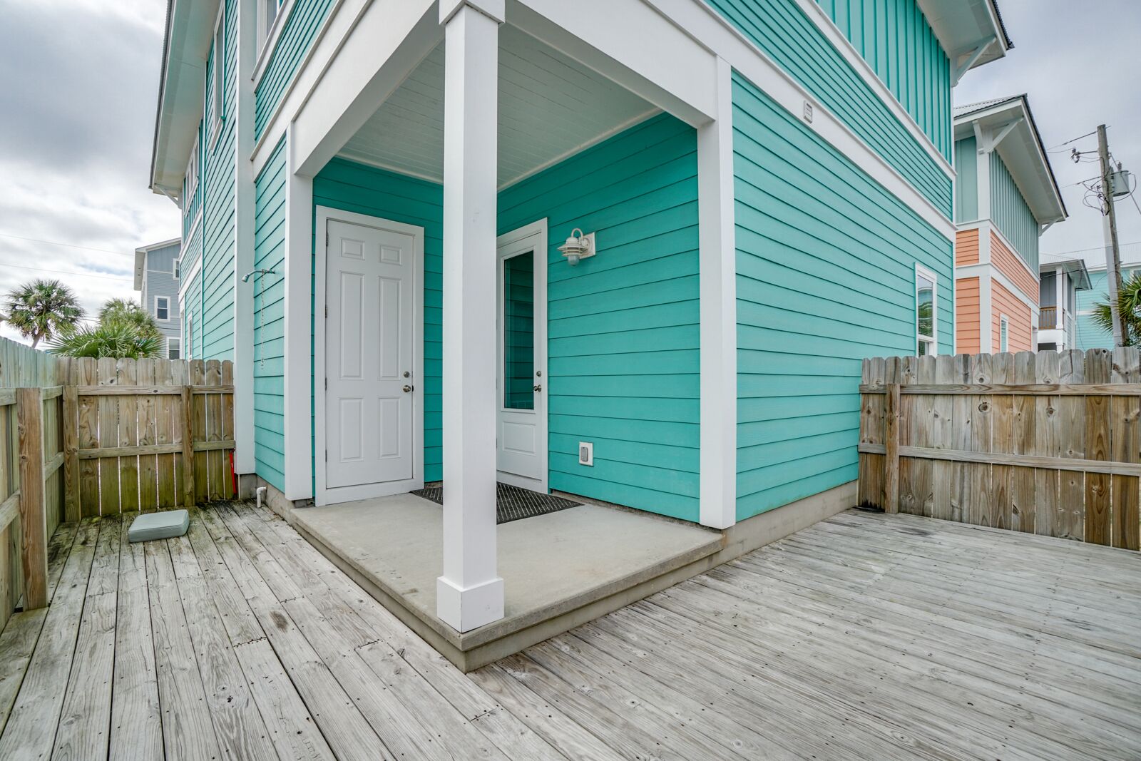 A turquoise house with a white porch and a wooden deck.