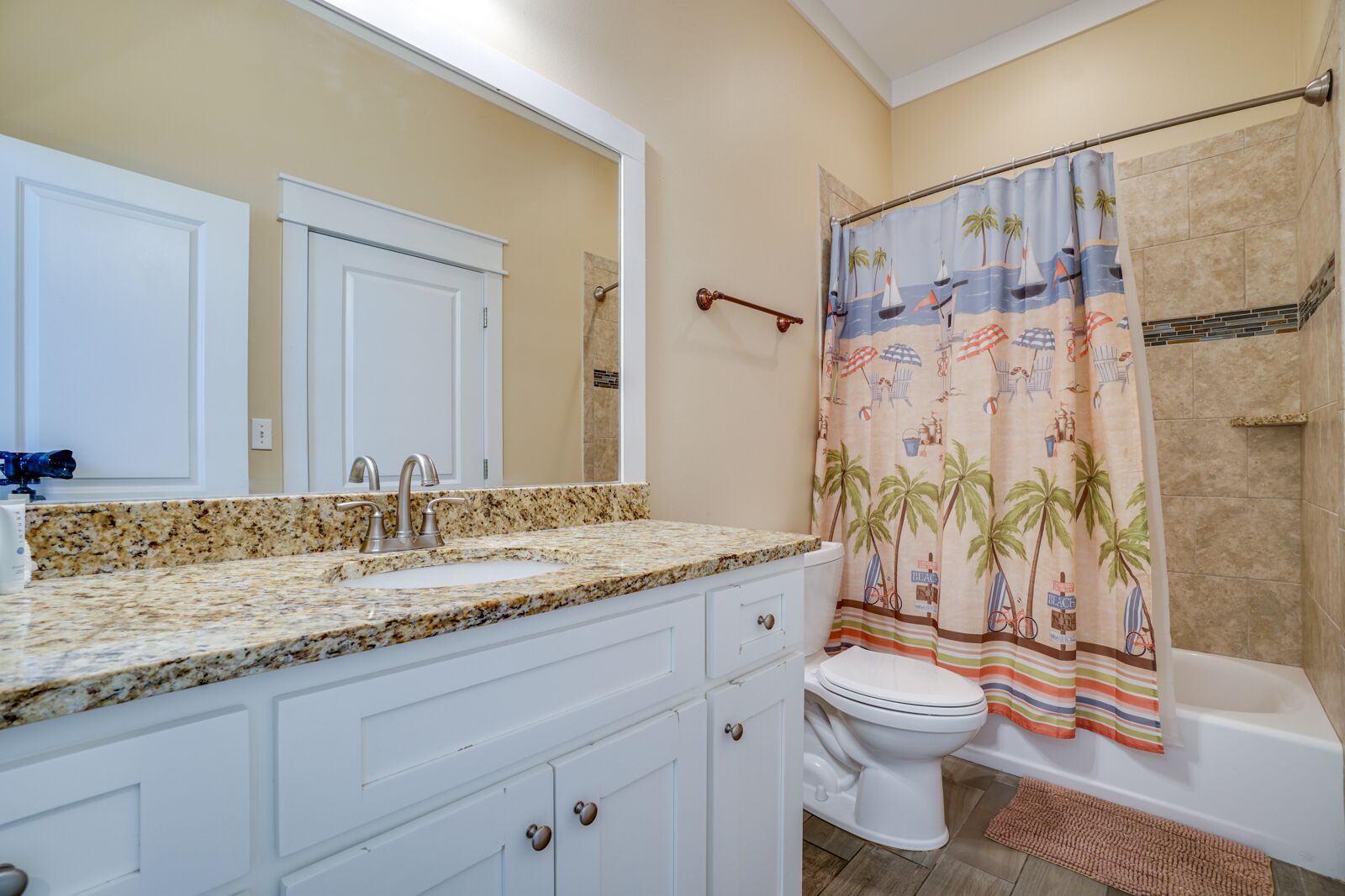 A bathroom with a granite countertop sink, a white toilet, and a shower curtain with a beach theme.