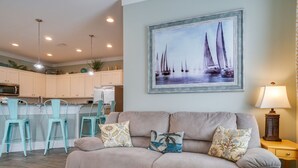 A living room with a beige sofa, teal chairs, and a painting of sailboats. - Sea Escape! Stunning Gulf-View Retreat with Private Pool (Panama City Beach)