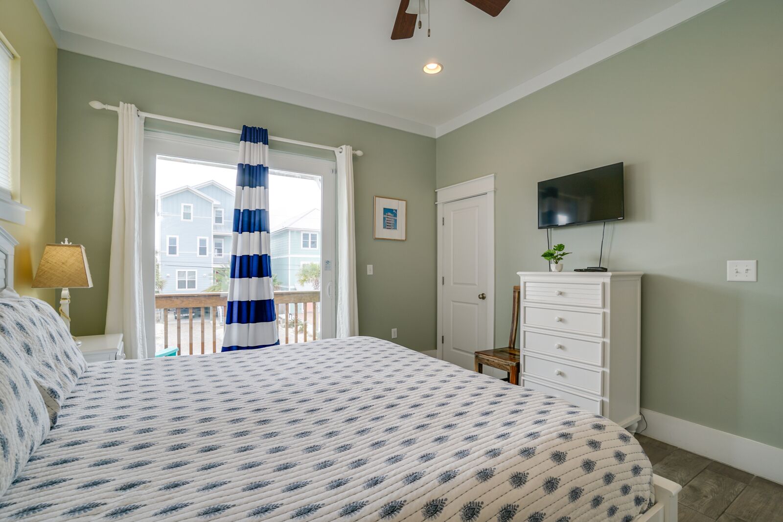 A bedroom with a bed, a dresser, a television, and a window with curtains.