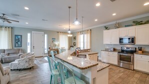 A spacious living room with a large sofa and matching chairs, a kitchen with white cabinets and stainless steel appliances, and a dining area with a marble island and chairs. - Sea Escape! Stunning Gulf-View Retreat with Private Pool (Panama City Beach)