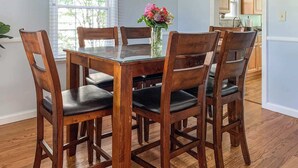 Een eetgedeelte met een houten tafel en stoelen, een vaas met bloemen, en uitzicht op de keuken.