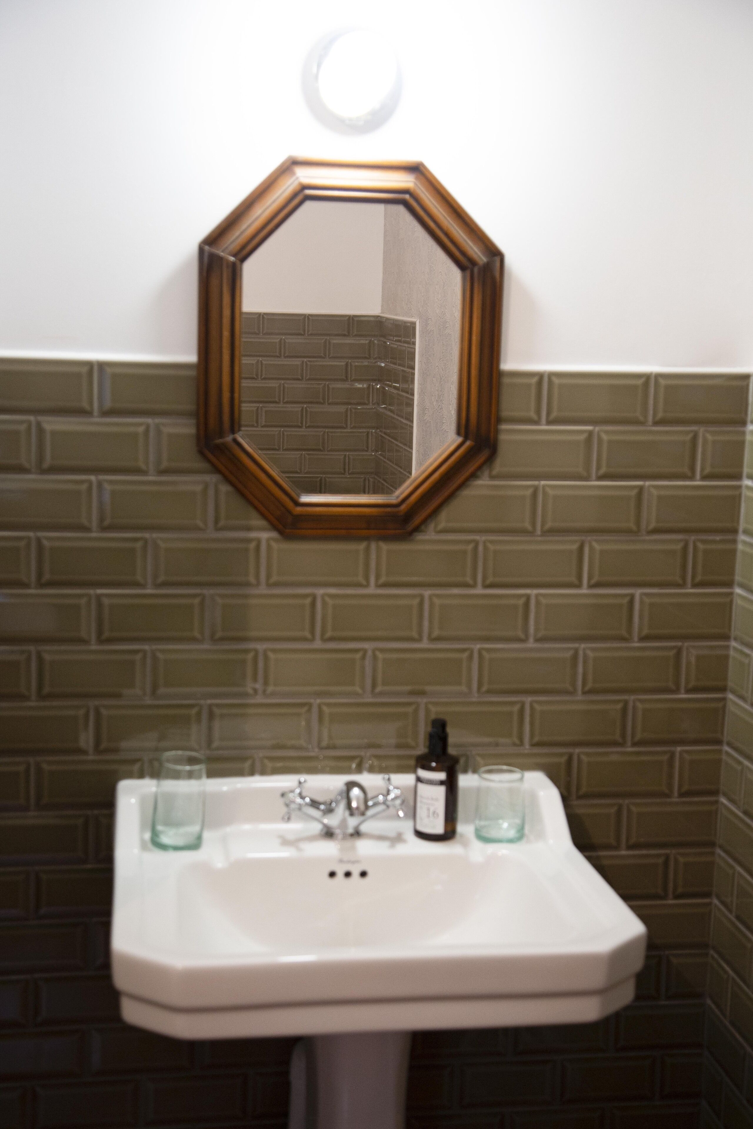 Een badkamer met een wit wastafel, een spiegel en een betegelde muur.