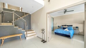 Une chambre moderne avec un grand lit, un banc et un escalier doté de rampes en métal.