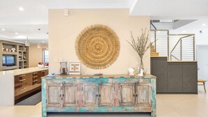 Une cuisine moderne avec un îlot central en bois rustique, une grande tapisserie murale tissée et un escalier doté d’une rampe en verre.