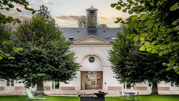 A building with a central arched entrance, surrounded by a well-maintained lawn and two large trees.