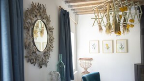 A room with a blue chair, a mirror, and a wall with framed botanical prints.