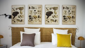 A neatly made bed with white and colored pillows, a woven headboard, and three botanical posters on the wall.