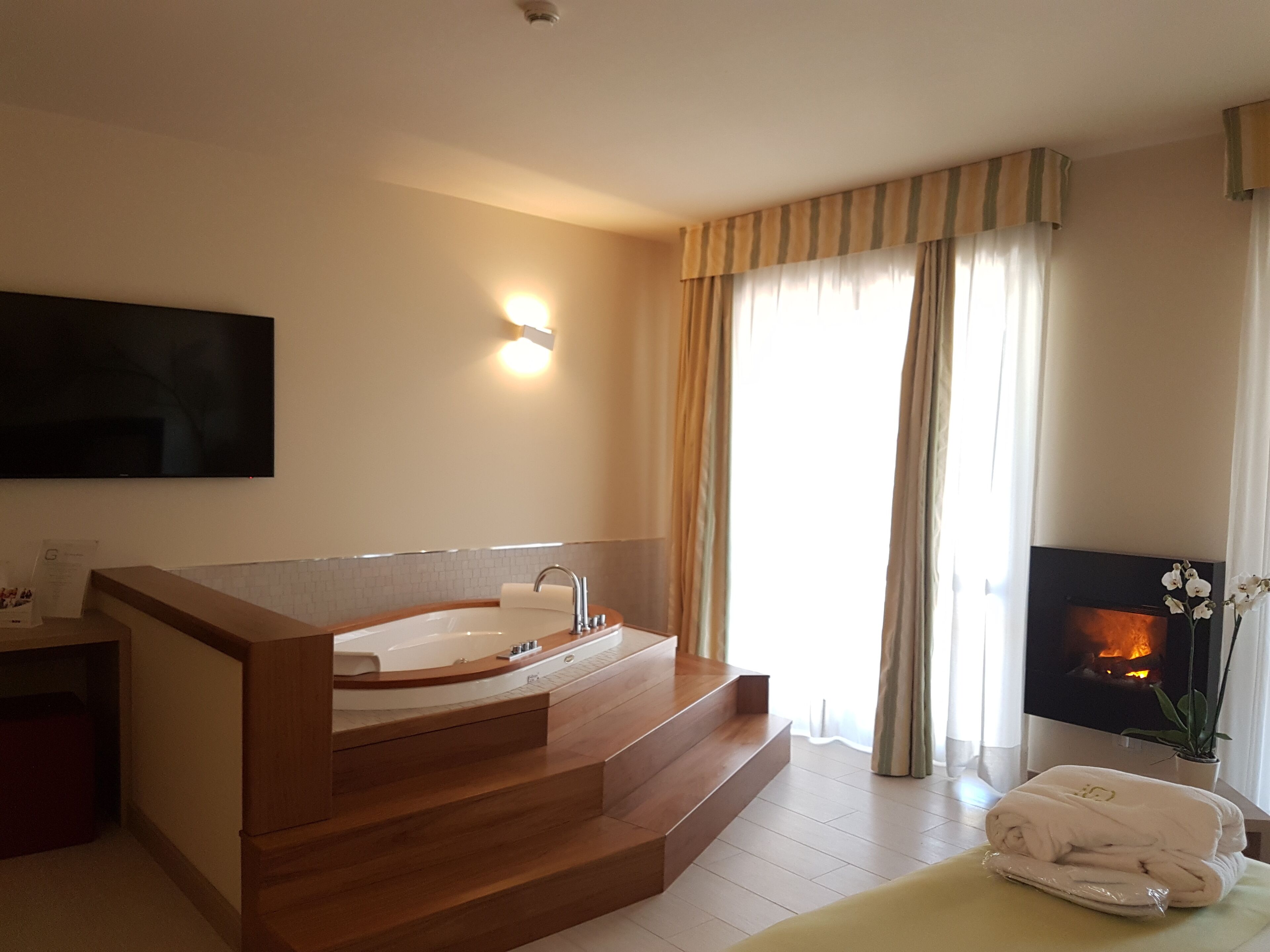 Un baño moderno con una bañera independiente, un tocador de madera, un televisor de pantalla plana en la pared y una chimenea con una planta en maceta.