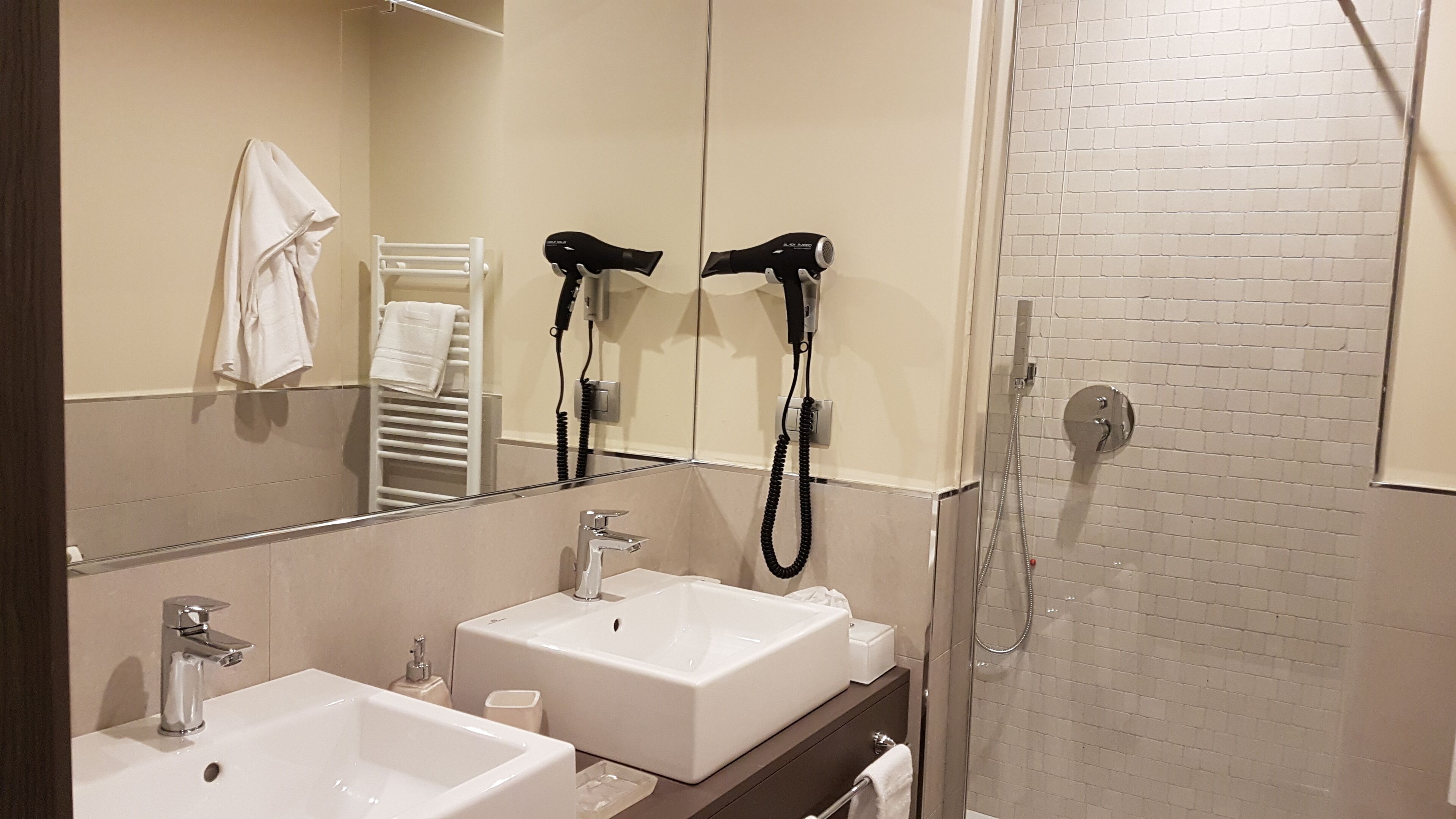 A modern bathroom with two sinks, a mirror, a towel rack, and a hairdryer.