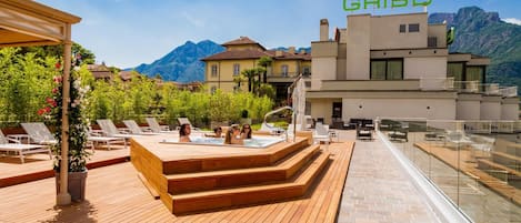 A rooftop terrace with a hot tub, lounge chairs, and a view of mountains.
