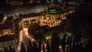 Un hotel de varios pisos con un llamativo letrero 'GRISO', que cuenta con un patio central con una fuente, rodeado de áreas ajardinadas y árboles altos.