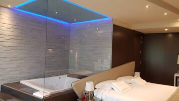 A modern hotel room with a large bed, a glass-enclosed jacuzzi, and a dark wooden headboard.