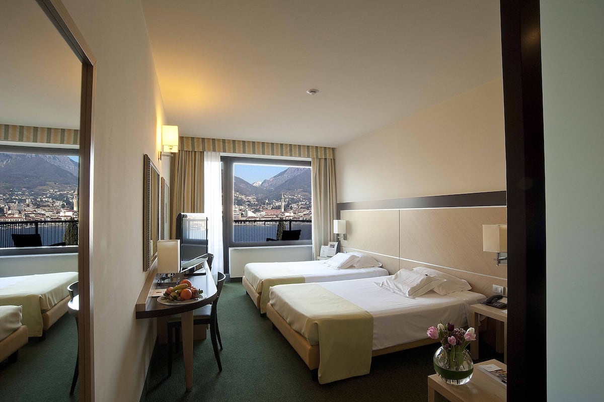 A hotel room with two beds, a desk, a chair, and a view of a city and mountains.
