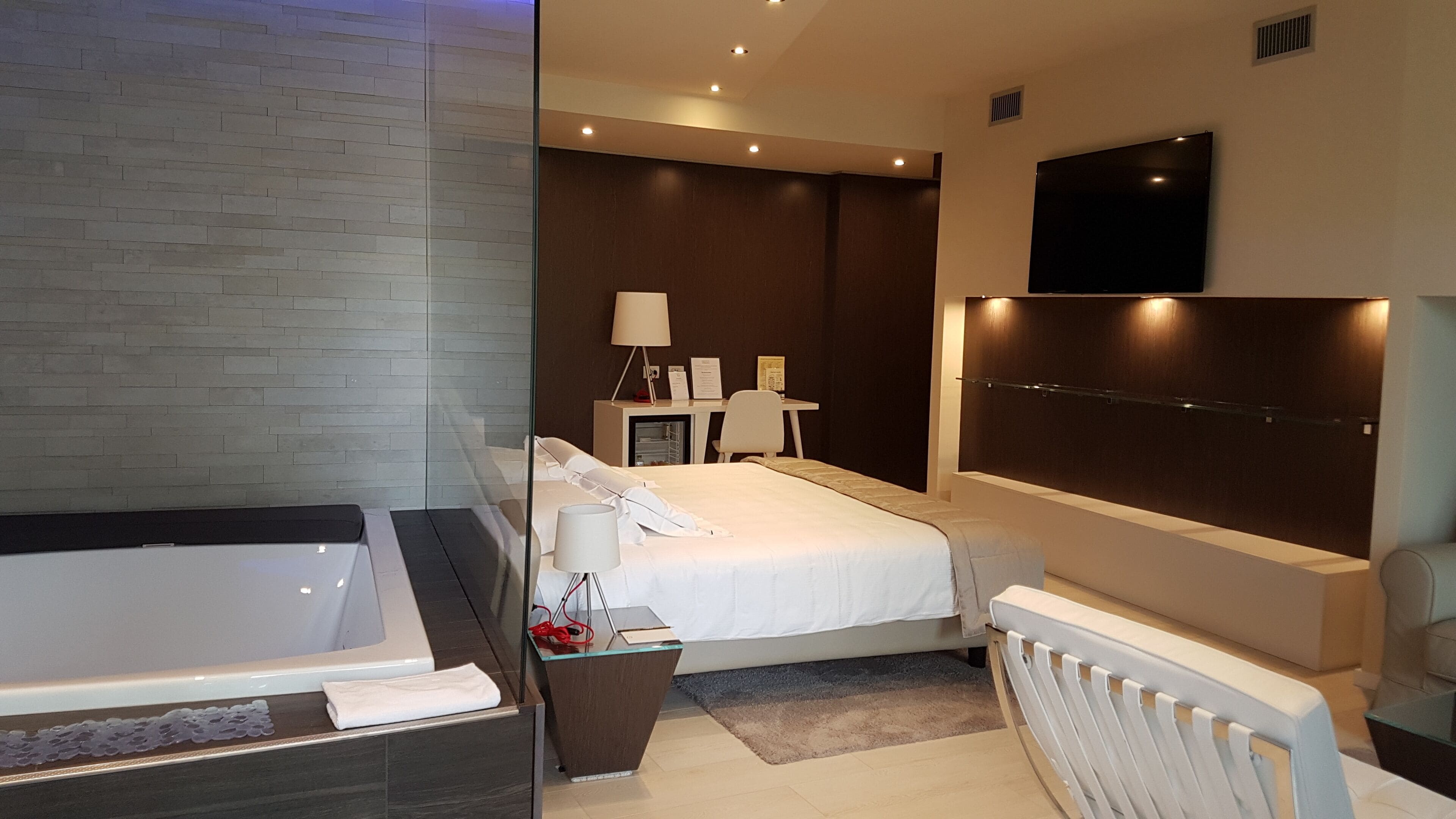 Une chambre d’hôtel moderne dotée d’un grand lit, d’une salle de bain séparée avec baignoire, d’un bureau avec une chaise et d’un téléviseur à écran plat fixé au mur.
