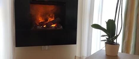A modern living room with a fireplace, a wooden side table, and a potted plant.