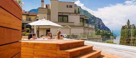 A modern outdoor seating area with wooden steps and a white umbrella, overlooking a mountainous landscape.