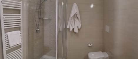 Een moderne badkamer met een douche met glazen wand, een wit toilet en een zwart wastafelmeubel met toiletartikelen.