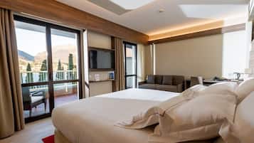 Habitación de hotel con una cama grande, televisión, sofá y balcón con vistas a la montaña.