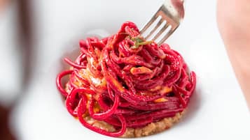 Un plato blanco con una porción de pasta cubierta de rodajas de remolacha roja.