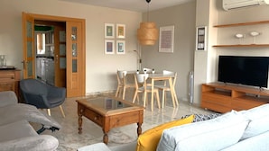 Una sala de estar con sofá, mesa de centro, mueble para televisión y comedor con sillas y una mesa.