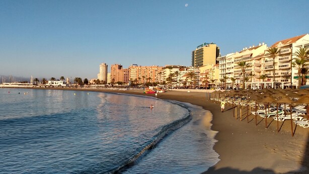 Un hotel frente a la playa con vistas al mar, un paseo marítimo y palmeras.