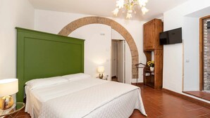 A bedroom with a green headboard, a bed with white bedding, a TV mounted on the wall, and a wooden cabinet.