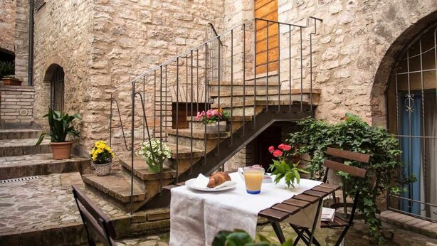 A stone building with a staircase, outdoor seating area, and potted plants.