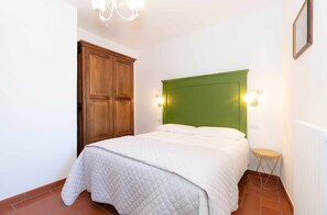 Un dormitorio con cama, armario de madera, cabecero verde y dos luces fijadas a la pared.