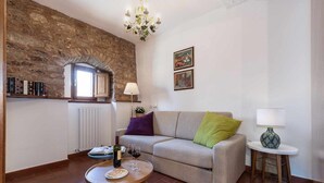 A living room with a stone wall, a sofa, a round table with a bottle and glasses, and a small side table with a lamp.