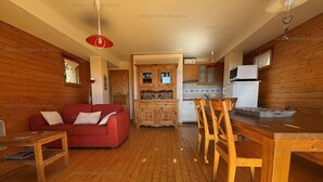 Un intérieur chaleureux avec des éléments en bois, notamment un canapé rouge, une table à manger en bois et des chaises. On aperçoit au fond une cuisine équipée de placards et d’un four à micro-ondes.