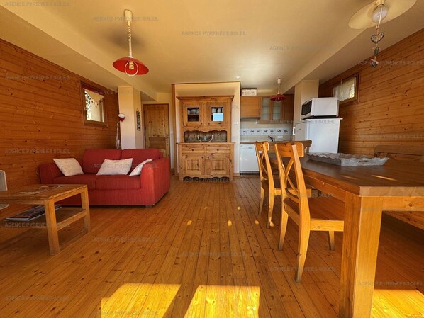 A cozy wooden interior with a red sofa, wooden dining table, and chairs. A kitchen with cabinets and a microwave is visible in the background. - F4 chalet base with terrace and parking - Les Angles (Les Angles)