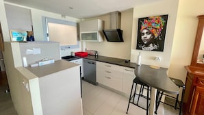 Cocina moderna con refrigerador integrado, microondas y lavamanos. Zona de comedor con una silla y una mesa.