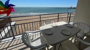 Un balcón con una mesa dispuesta para dos, con vista a una playa y un muelle a lo lejos.