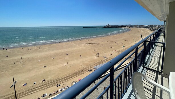 Vista a la playa desde un balcón con barandilla, cielo despejado y el océano.