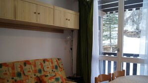 A room with a sofa, a dining table, and a window with a view of trees. - Bright studio in Pra Loup 1500 for 4/5 people, easy ski lift access (Pra-Loup)