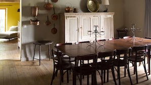 Un comedor con mesa y sillas de madera, un armario blanco con ollas colgantes, y luces colgantes.