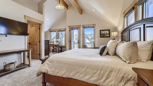 A bedroom with a large bed, wooden headboard, and a desk with a chair. There is a window with a view of a house and a door leading to another room. - Awesome Townhome just off Main Street in Frisco!! (Frisco)