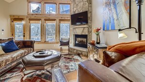 A cozy living room with a stone fireplace, large windows, a flat-screen TV, and a comfortable seating area. - Awesome Townhome just off Main Street in Frisco!! (Frisco)
