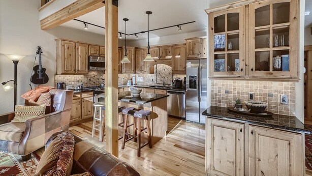 A spacious kitchen with wooden cabinets, a stainless steel refrigerator, and a dining area with a bench and stools. - Awesome Townhome just off Main Street in Frisco!! (Frisco)