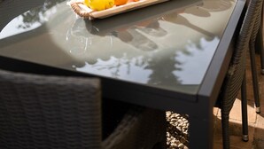 Une table à manger avec des chaises en osier, une bouteille de vin, un vase rempli d’herbe des pampas et un plateau de fruits.