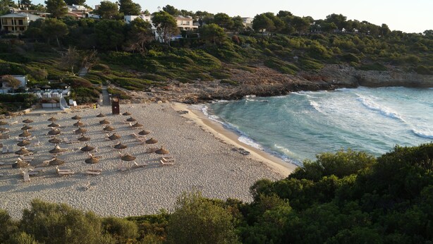 Une plage avec des parasols et des chaises longues, un rivage rocheux et des maisons en arrière-plan.