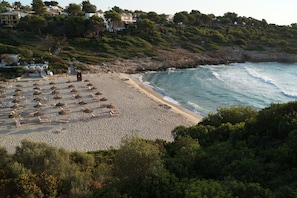Una playa con sombrillas y sillas reclinables, un litoral rocoso y casas al fondo.