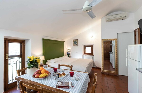 Habitació amb llit, taula de dinar amb esmorzar, ventilador de sostre i zona de cuina.