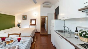 Kompakti hotellihuone, jossa on sänky, pieni ruokapöytä aamiaisineen, pieni keittiönurkkaus ja kylpyhuone, joka näkyy oven läpi.